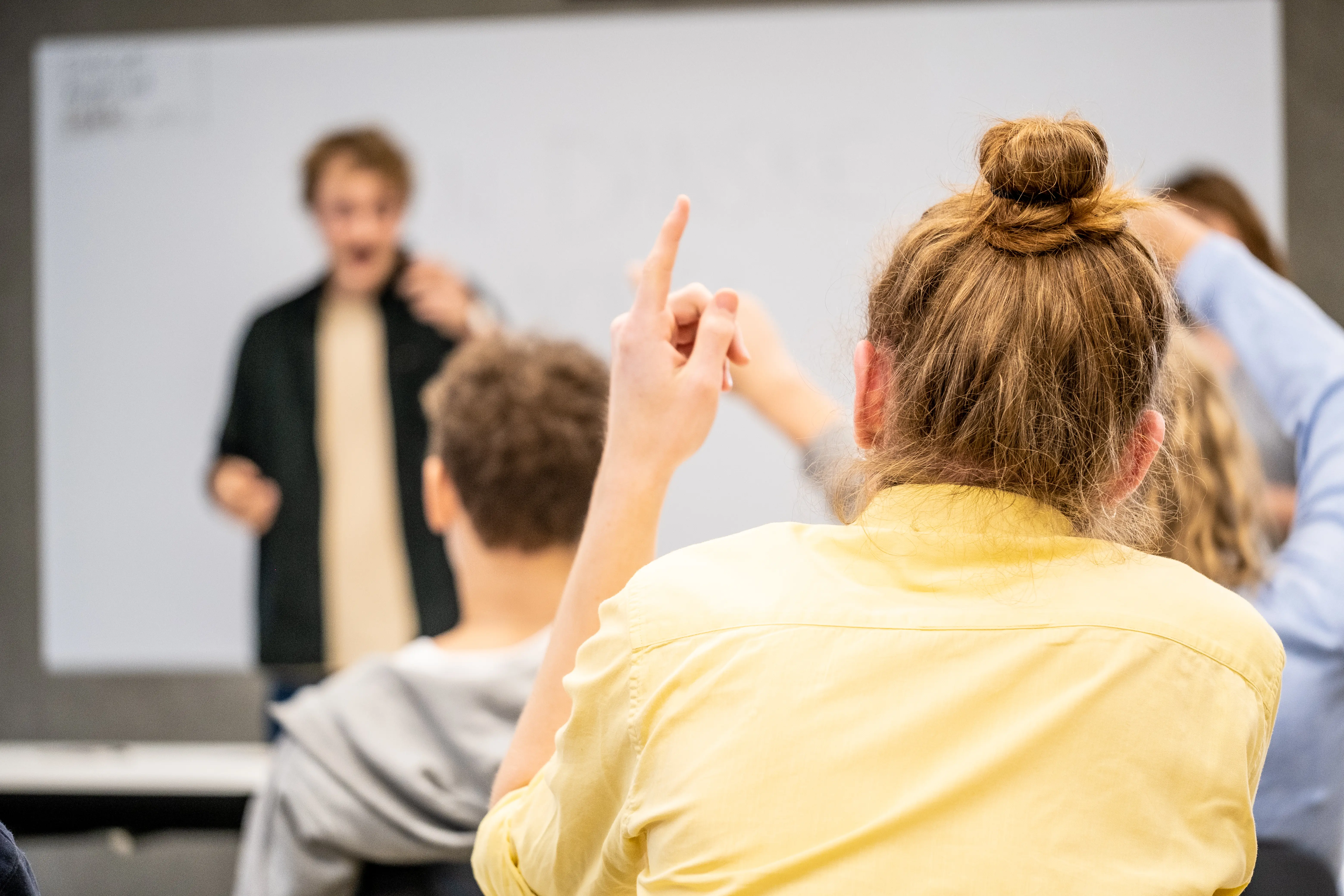 Ung person rækker hånden op under et skolebesøg fra Jobpatruljen, mens andre unge lytter i et undervisningslokale.